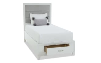 White bedroom furniture set including a dresser with mirror, nightstand with lamp, upholstered headboard bed with storage drawer, and chest of drawers, featuring modern silver handles and a clean, minimalist design.