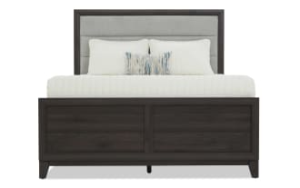 Dark wood bedroom set featuring a king-size bed with upholstered gray headboard, six-drawer dresser with mirror, and two-drawer nightstand with lamp.