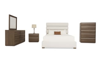 Modern bedroom furniture set with a cream upholstered bed featuring a padded headboard, wooden dresser with mirror, matching nightstand with lamp, and tall chest of drawers in walnut finish.