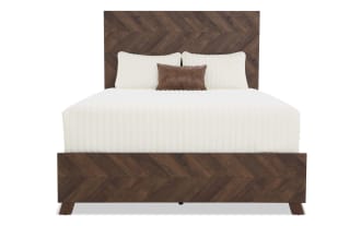 King-size bed with dark brown chevron-patterned wooden frame and headboard, featuring white quilted bedding and a small brown leather accent pillow.