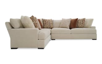 Beige fabric L-shaped sectional sofa with plush cushions and a mix of patterned and solid rust-colored throw pillows, modern design.