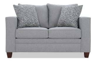 Gray fabric loveseat with two patterned gray and white throw pillows, featuring a modern design with wooden legs and plush cushions.