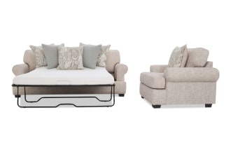 Beige fabric sofa bed with rolled arms and dark wooden legs, featuring a pull-out mattress and decorative paisley and solid gray cushions.