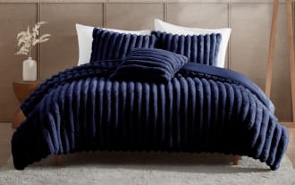 Luxurious navy blue plush ribbed comforter set on a wooden bed frame with matching textured pillows, styled in a modern bedroom.