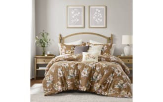 Bed with floral brown comforter set, beige upholstered wooden headboard, matching pillows, wooden nightstand, and natural light from window in cozy bedroom.
