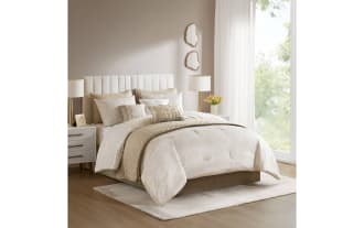 Beige and cream quilted bedding set on a modern upholstered bed with matching pillows, nightstands, and lamps in a bright bedroom.