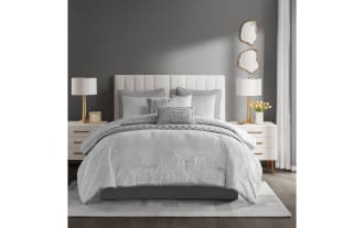 Gray textured bedding set on a bed with a white upholstered headboard, featuring multiple pillows, quilted comforter, and matching shams in a modern bedroom.