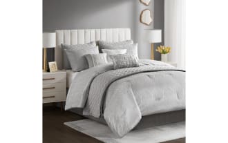 Gray textured bedding set on a bed with a white upholstered headboard, featuring multiple pillows, quilted comforter, and matching shams in a modern bedroom.