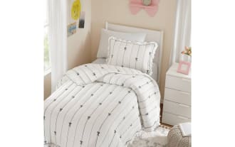 White comforter set with black vertical lines and bow patterns, featuring ruffled edges, on a twin bed in a cozy bedroom setting.