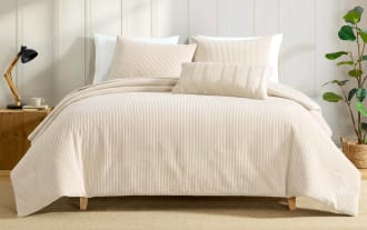 Beige ribbed velvet comforter set with matching pillow shams and decorative pillow on a wooden platform bed in a modern bedroom.