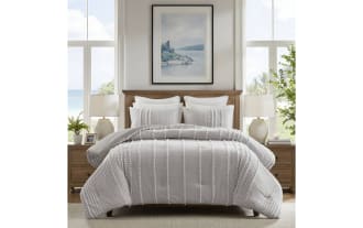 Gray textured comforter set with vertical tufted stripes, matching pillow shams, white pillows, wooden headboard, and bedside tables with lamps in a bright bedroom.