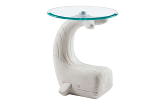 White wooden side table shaped like a whale with a curved tail supporting a round clear glass top, modern nautical decor.
