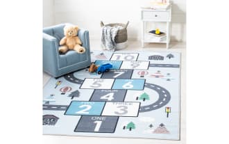 Happy Hopper 3' x 5' light blue transitional area rug with playful road and number block pattern in gray, white, and blue. Made of soft, washable polyamide fabric with slip-resistant backing, ideal for kids' playrooms.