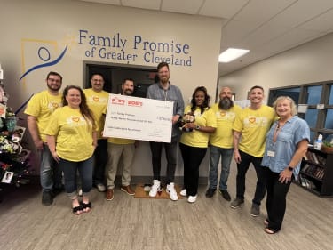 Group of volunteers from Bob’s Outreach presenting a $37,000 donation check to Family Promise of Greater Cleveland, standing in front of a wall with the organization’s logo.