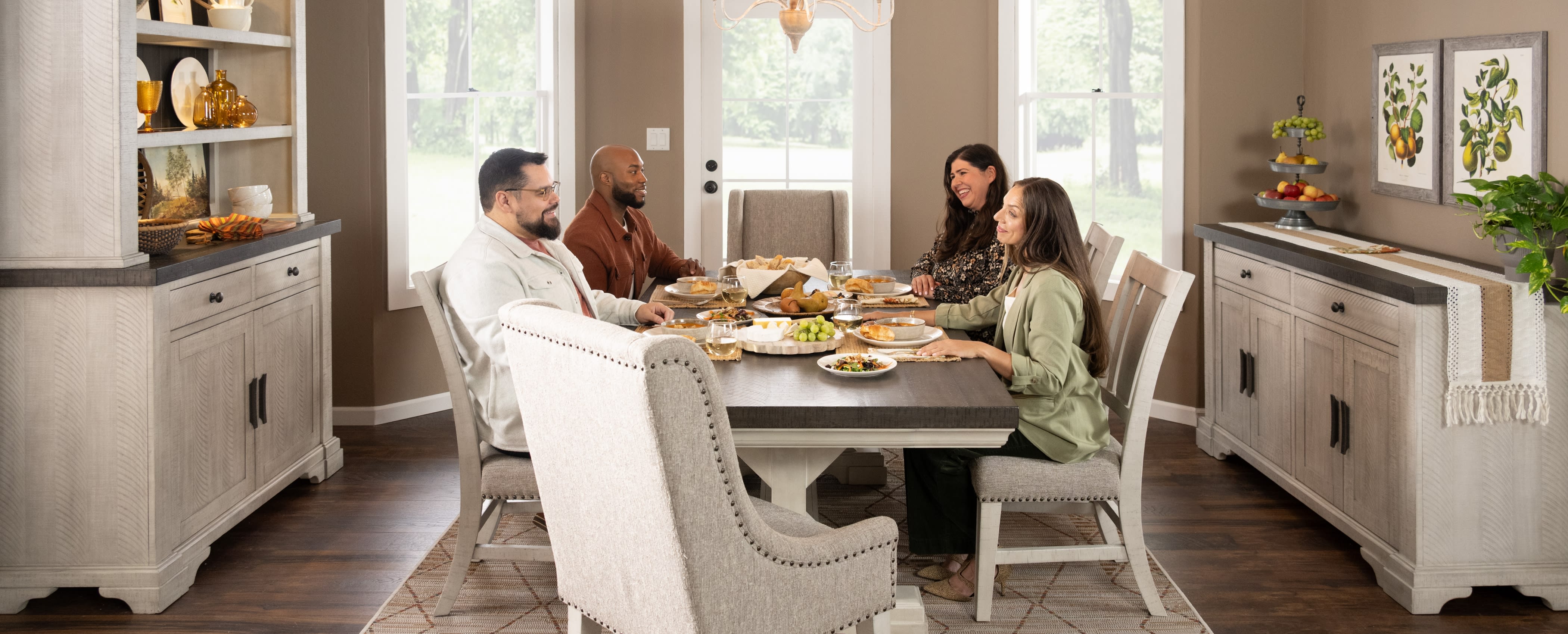 Four adults sit around Beaumont dining table set with food, sharing a meal together in a well-lit room with large windows
