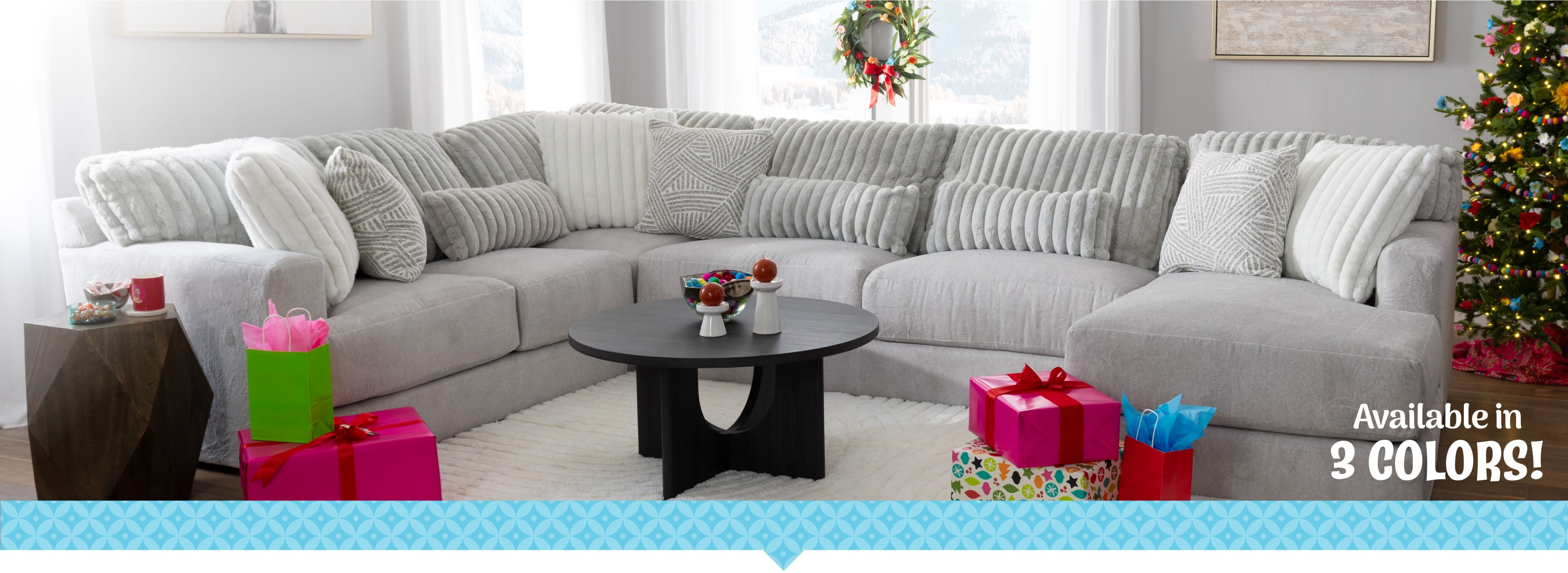 A large light gray sectional sofa in a bright living room, with wrapped presents and holiday decor. Text reads, “Available in 3 colors!”.