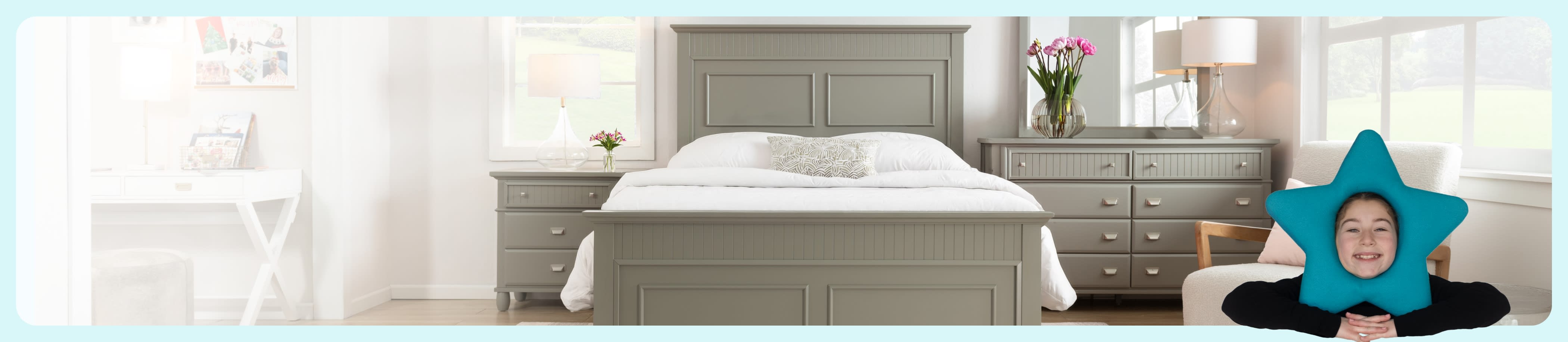 Bright bedroom with gray furniture, including a bed, nightstand, and dresser. A pink orchid and lamp adorn the dresser. Soft natural light fills the room.