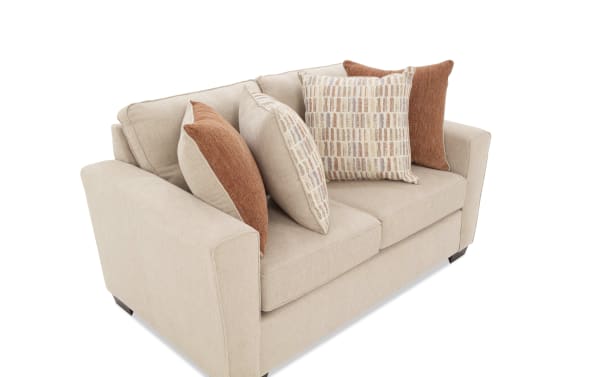 Beige fabric loveseat sofa with wide armrests, dark wooden legs, and four decorative throw pillows in rust and patterned beige tones.