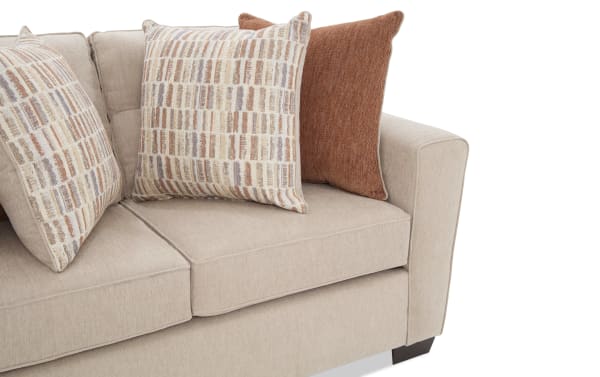 Beige fabric sofa with square armrest, featuring two patterned beige and rust-colored throw pillows and one solid rust-colored pillow, showcasing a modern, cozy living room style.