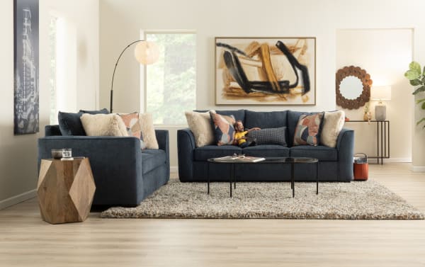 Transitional Brynn collection navy blue fabric sofas with plush polyester upholstery, decorative pillows, and a geometric wooden side table in a modern living room.