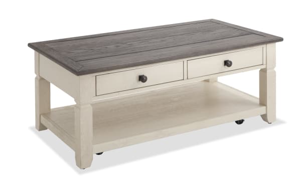 Laurel White & Brown Storage Coffee Table with two-tone distressed acacia veneer top, white rubberwood base, black hardware, two drawers, bottom shelf, and casters in cottage style.