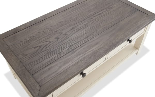 Two-tone Laurel White & Brown Storage Coffee Table in cottage style with dark hardware, distressed acacia veneer top, two drawers, and bottom shelf.