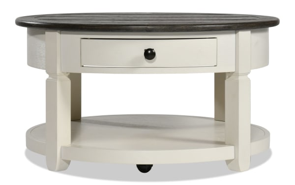 Laurel White & Brown Round Storage Coffee Table from Laurel Entertainment & Occasional collection, farmhouse style MDF wood with two-tone finish, distressed dark brown top, white base, black knob drawer, and lower shelf for living room storage.
