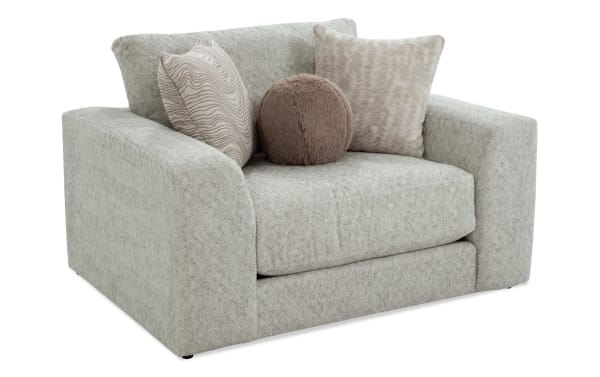 Light gray fabric armchair with wide square arms, plush seat cushion, and three decorative pillows in beige and brown tones, showcasing a modern cozy design.