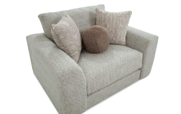Modern light gray fabric loveseat with wide armrests, featuring two square patterned throw pillows and one round plush brown pillow.