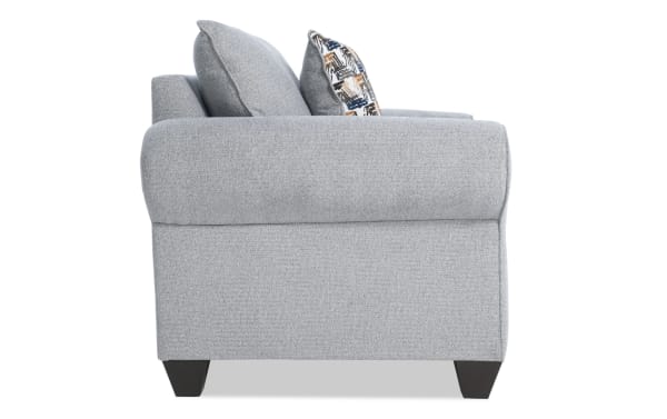 Gray Kylie Gray Chair side view showcasing transitional style with plush polyester fabric upholstery, rolled arms, tapered dark wood legs, and accent pillows.