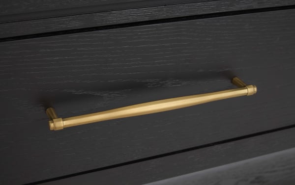 Matte gold metal drawer handle with a sleek, straight design mounted on a dark wood textured drawer front, suitable for modern cabinetry.