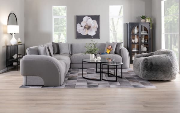 Contemporary Gravity Gray Curved Ottoman in polyester fabric with plush, feather-blend topper, paired with matching modular sectional and glass nesting tables.