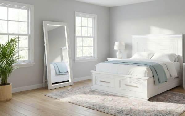 Modern bedroom with white wooden bed frame featuring storage drawers, matching nightstands, a large standing mirror, light gray walls, and hardwood flooring.