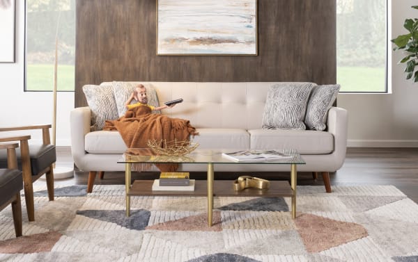 Mid-century modern beige faux leather sofa with tufted back, wooden legs, and patterned accent pillows in a stylish living room setting.