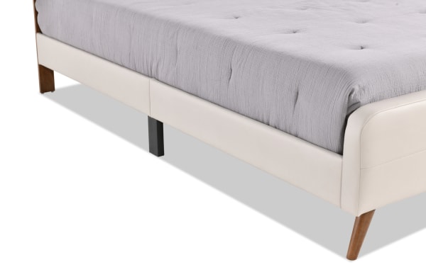 Cream Bettie Twin platform bed with mid-century modern tapered wooden legs, cream faux leather vinyl upholstery, and tufted mattress edge.