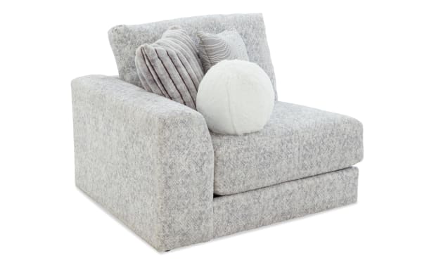 Modern light gray fabric armchair with thick cushions and three decorative pillows, including a round white faux fur pillow, designed for living room comfort.