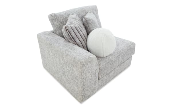 Modern gray fabric armchair with wide armrests, plush cushions, and three decorative pillows in gray and white faux fur, ideal for cozy living room seating.