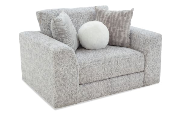 Gray upholstered loveseat with thick cushions and wide armrests, featuring three decorative pillows in textured gray and white faux fur.