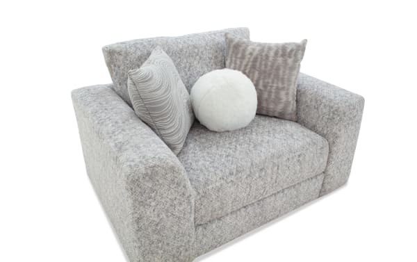 Gray fabric loveseat with thick armrests and backrest, featuring two square patterned pillows and one round white fluffy pillow, suitable for modern living rooms.
