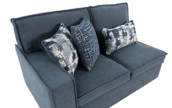 Blue fabric loveseat sofa with thick cushions and three decorative patterned throw pillows in navy and white, modern living room furniture.