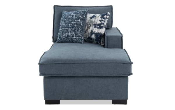 Blue fabric chaise lounge with two patterned blue and gray throw pillows, featuring cushioned armrest and backrest, modern style.