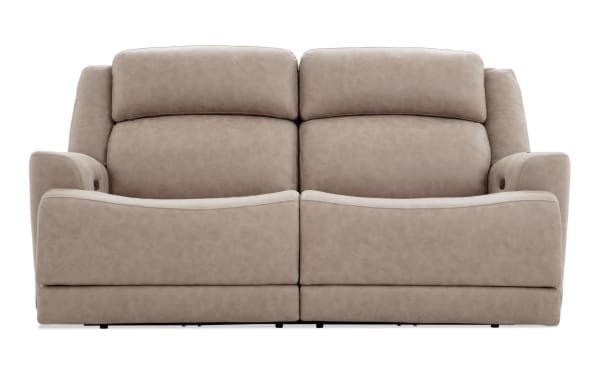 Beige leather reclining loveseat with padded armrests and headrests, featuring a modern, comfortable design ideal for living room seating.