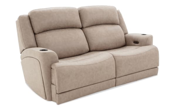 Beige leather reclining loveseat with padded headrests, cup holders, and built-in control buttons for adjustable comfort.