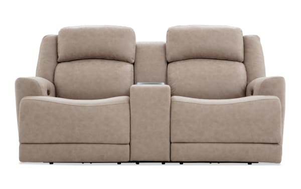 Beige leather reclining loveseat with center console and cup holders, featuring plush cushioned backrests and padded armrests for comfort.