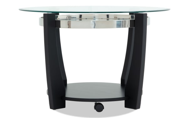 Round modern side table with black wooden legs, a lower black shelf, a chrome metal ring, and a clear glass top surface.