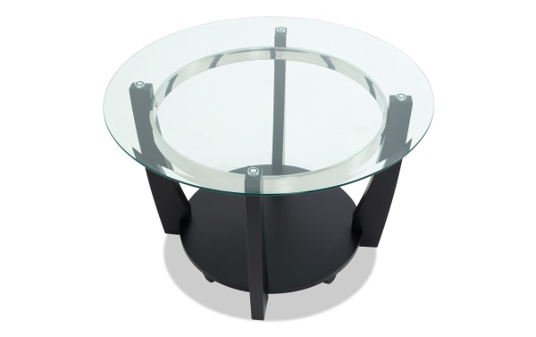 Round modern coffee table with clear glass top, black wooden legs, and circular lower shelf, featuring a sleek metal ring support.
