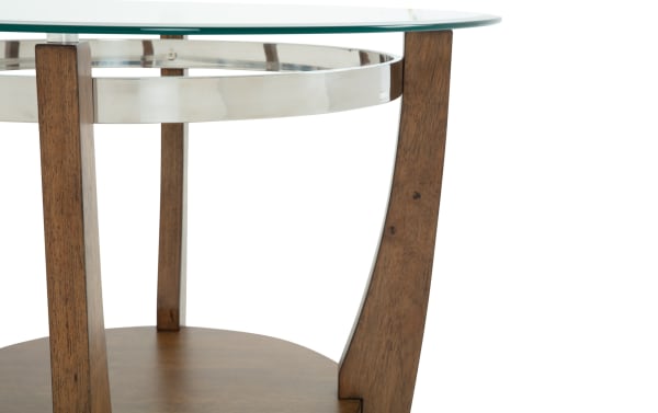 Close-up of a round side table with a clear glass top, polished metal rim, and curved wooden legs in a warm brown finish.