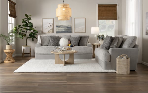 Modern living room with gray plush fabric sofas, wooden round coffee table, white area rug, woven pendant light, and natural decor accents.