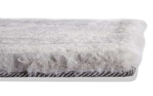Soft, light gray faux fur rug edge with a plush texture and black-and-white herringbone fabric backing, ideal for cozy home decor.