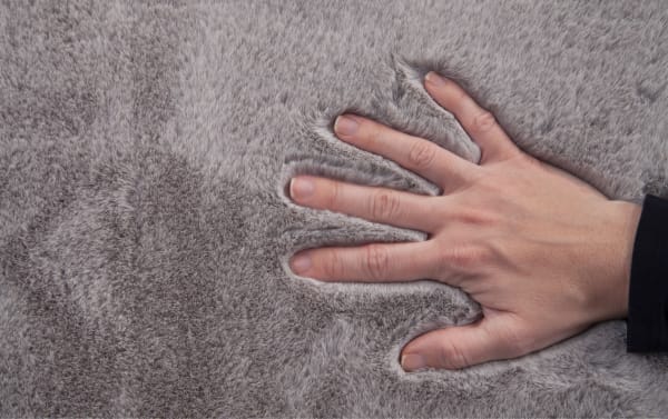 Hand pressing down on soft, thick gray faux fur fabric, highlighting its plush texture and dense pile for cozy home decor or clothing.
